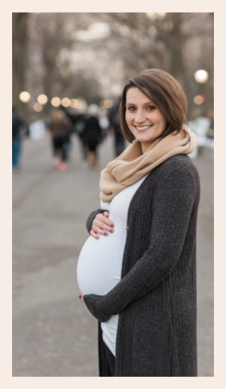 Picture of woman holding her baby bump while smiling towards the camera. 